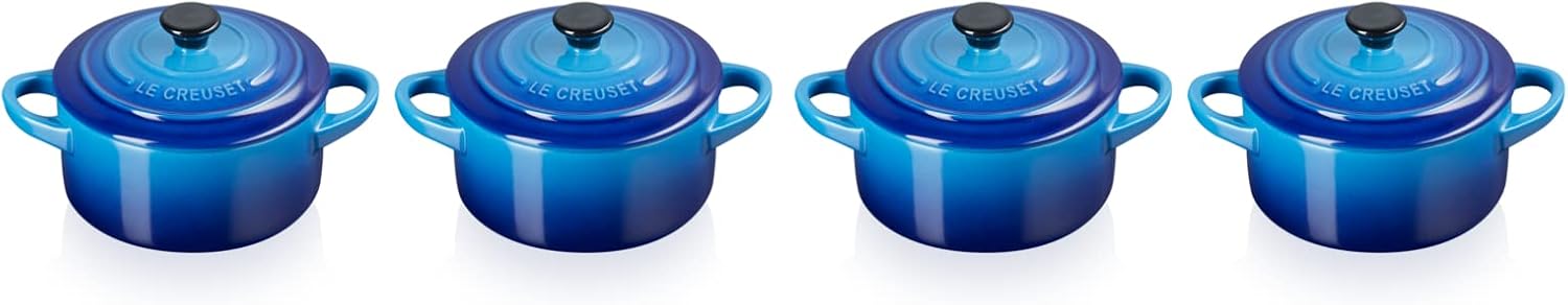 Four adorable Le Creuset azure stoneware mini casseroles—lids on, just waiting for your culinary magic. They look fab against the soft neutral backdrop, perfect for those single portions. Such a charming touch for any table, right?