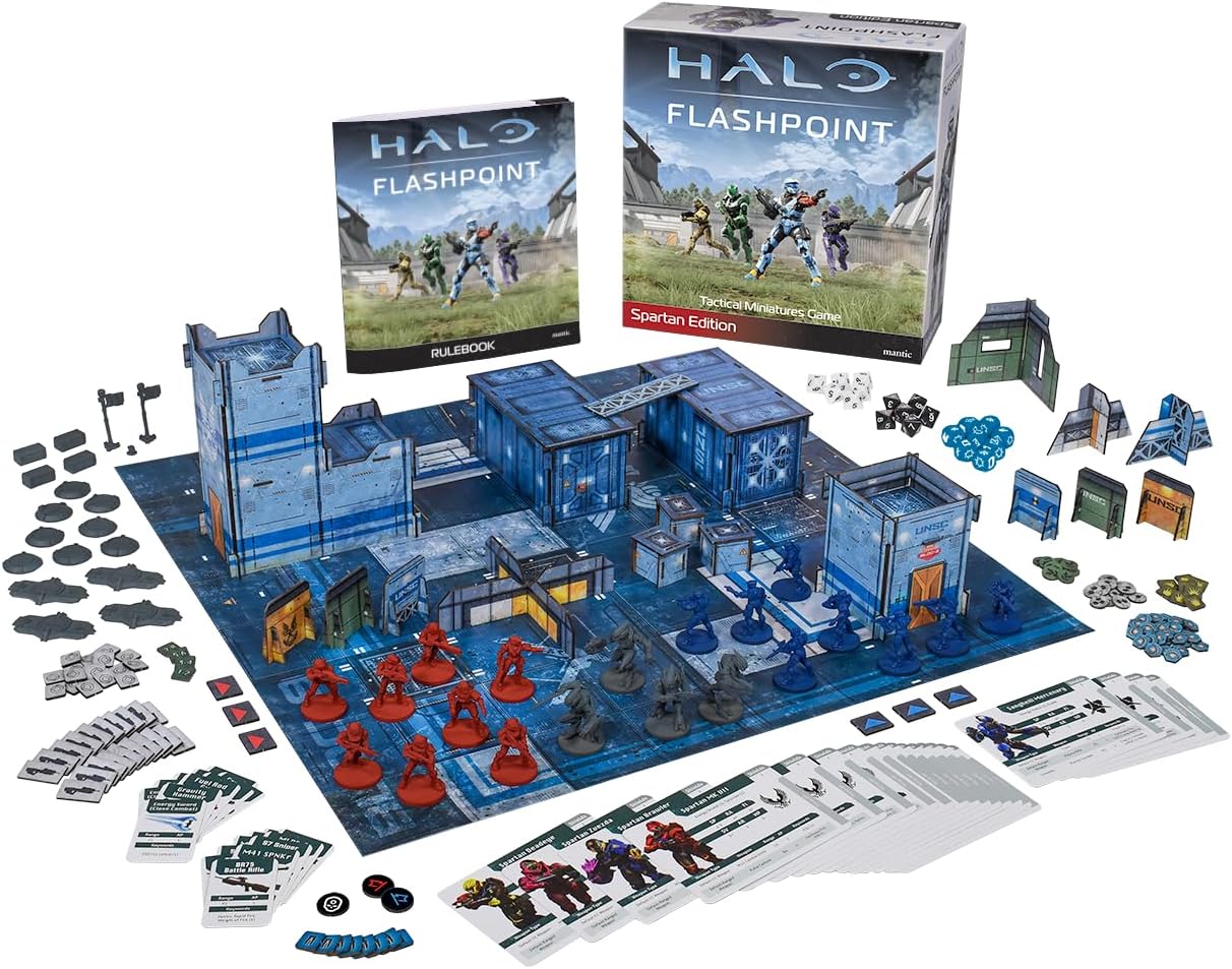 A lively mix of Halo Miniatures game gear sprawled across the tabletop—detailed plastic miniatures, vibrant playing cards, and those eye-catching terrain pieces all jumbled together. It's like a small battlefield ready for action, bursting with colour and personality.