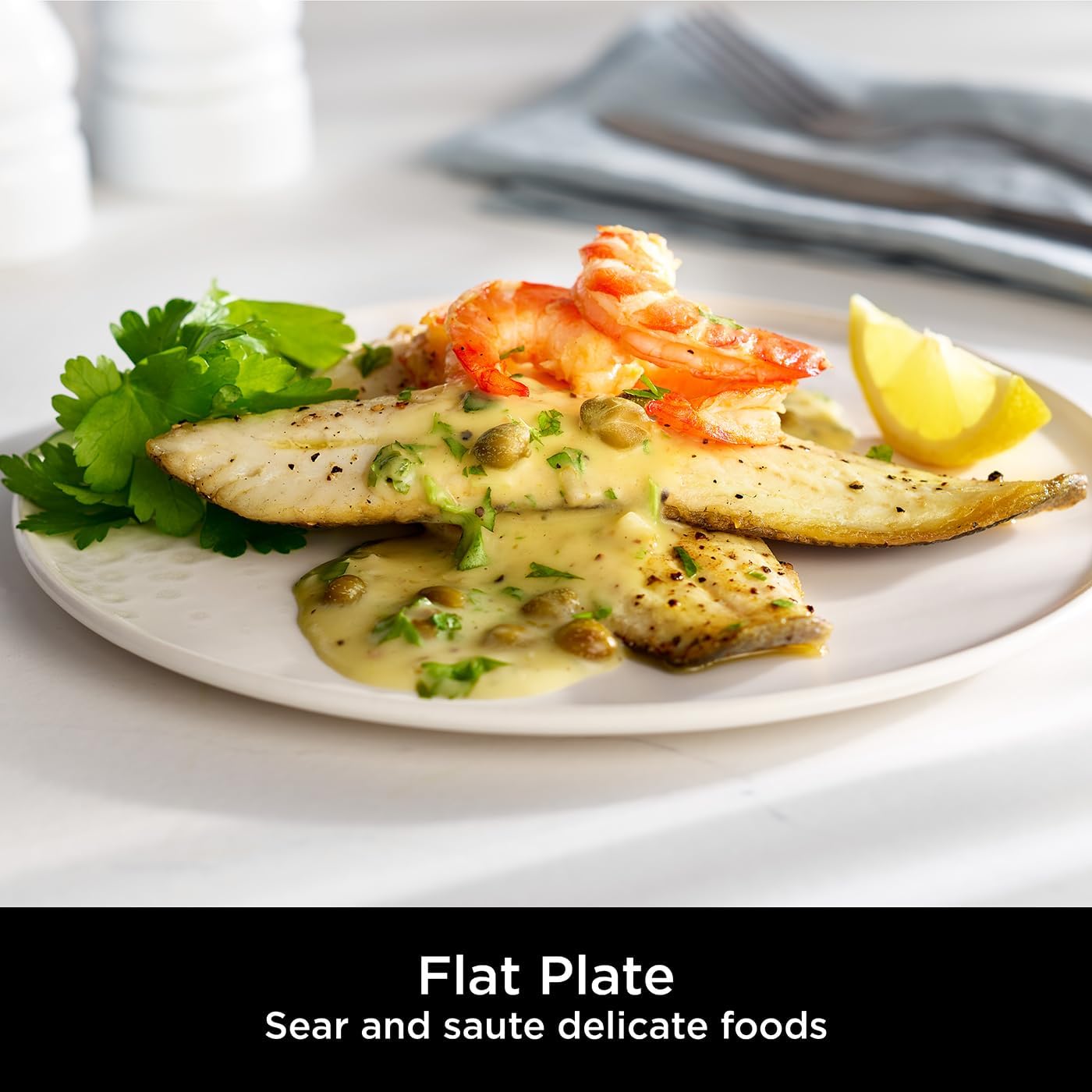 A compact Ninja Sizzle indoor grill—black as night—sits on a countertop, showing off its non-stick grill plate and handy mesh lid. Grease catch? Yep, that’s included too. Perfect for grilling without the fuss.