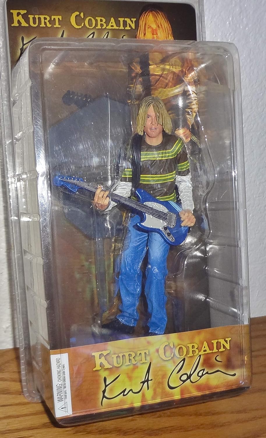 Kurt Cobain action figure—rocking that iconic grey sweater and jeans combo, clutching a guitar like it’s an extension of his soul. Pure nostalgia, against a crisp white backdrop; it just hits different.